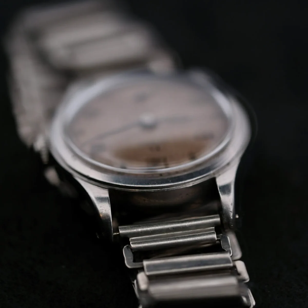 Close-up of an Omega WWII Era Military Sub Seconds watch with a slightly blurred wristwatch showcasing a metal bracelet and round dial. Positioned at an angle, the focus is on the left side, highlighting the textured links in this timeless pieces strap.