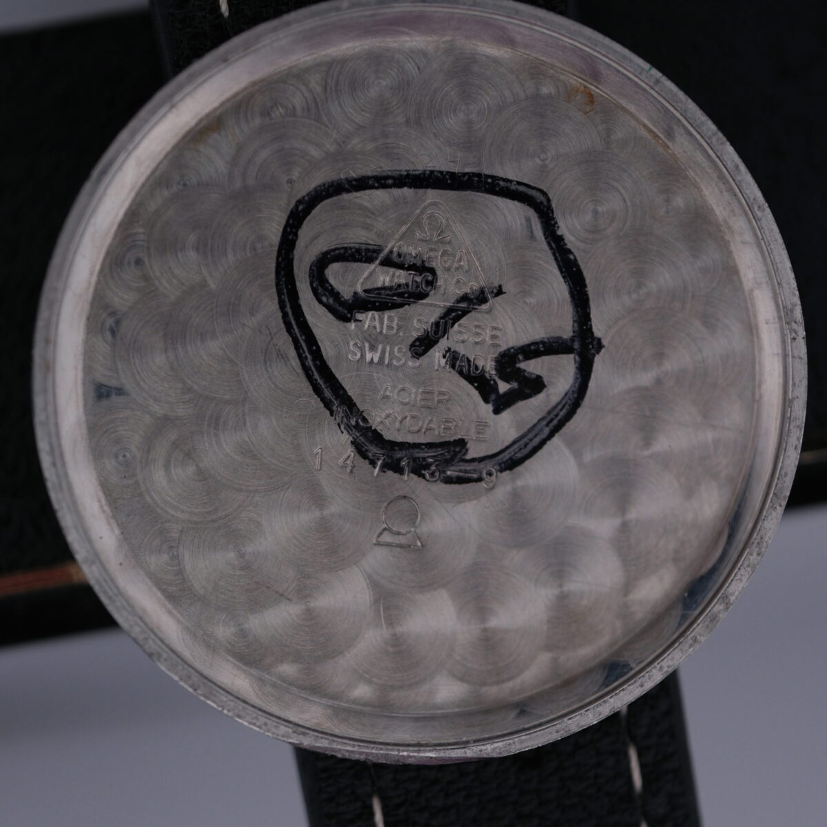 The Omega Manual Wind Cal. 268 watch case back features an engraving of the iconic logo with FAB. SUISSE, SWISS MADE, and ACIER INOXYDABLE, set against a decorative circular pattern, highlighting Omegas renowned craftsmanship.